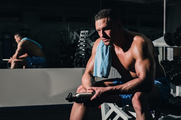 Sportivo senza camicia che riposa dopo l'allenamento presso il concetto di sport fitness in palestra