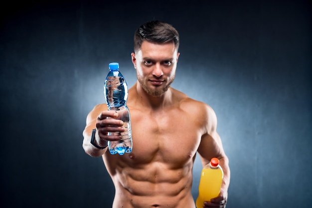 Sportivo sexy che tiene una bottiglia di acqua e soda Scelta tra bevanda sana e dannosa Ritratto Primo piano