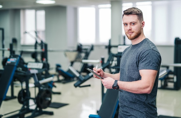 Sportivo sorridente in piedi in palestra leggera con attrezzature sportive e scrittura.