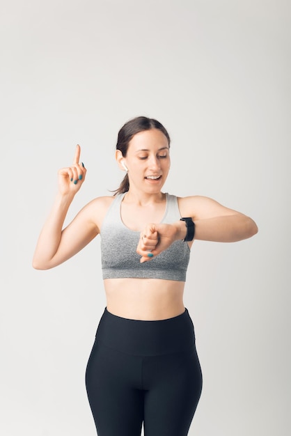 Sporty giovane donna guardando smartwatch e rivolto verso l'alto, su sfondo bianco