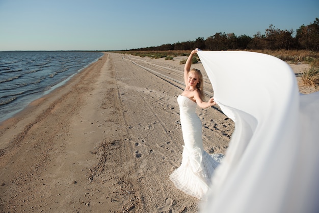 Sposa che cammina lungo la costa del mare che indossa bellissimo abito da sposa.