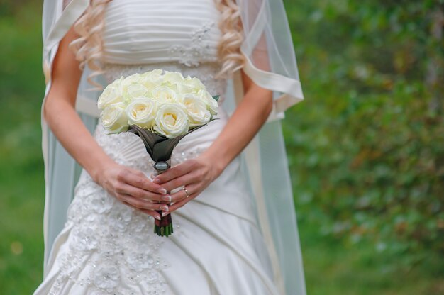 Sposa che tiene il mazzo di nozze bianco delle rose e del fiore di amore