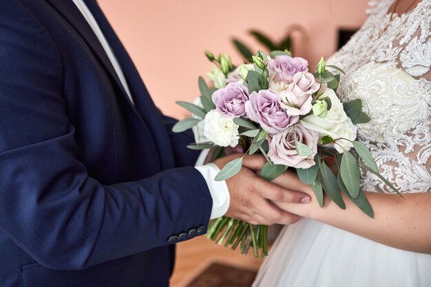 Sposa che tiene un bouquet da sposa nelle mani in piedi vicino allo sposo