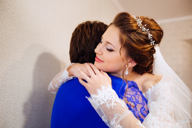 Sposa con bel trucco e acconciatura elegante abbraccia sua madre sullo sfondo del muro