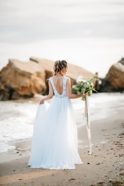 Sposa con un bouquet da sposa sulla riva del Mar Nero alla luce del tramonto