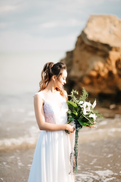 Sposa con un bouquet da sposa sulla riva del Mar Nero alla luce del tramonto