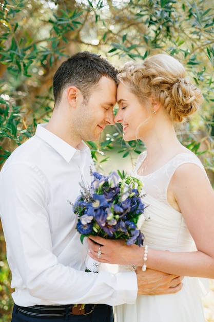 Sposa con un bouquet di fiori blu e lo sposo che si abbraccia teneramente nell'oliveto