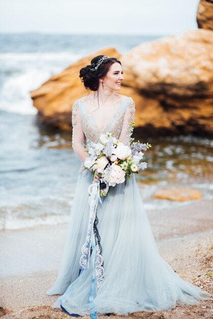 Sposa con un mazzo di fiori sulla spiaggia vicino all'acqua