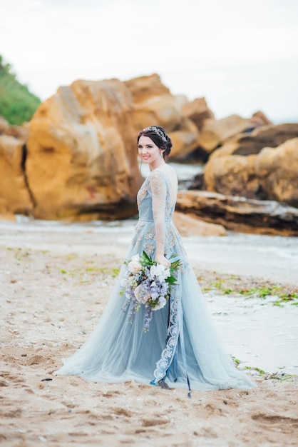 Sposa con un mazzo di fiori sulla spiaggia vicino all'acqua