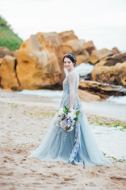 Sposa con un mazzo di fiori sulla spiaggia vicino all'acqua
