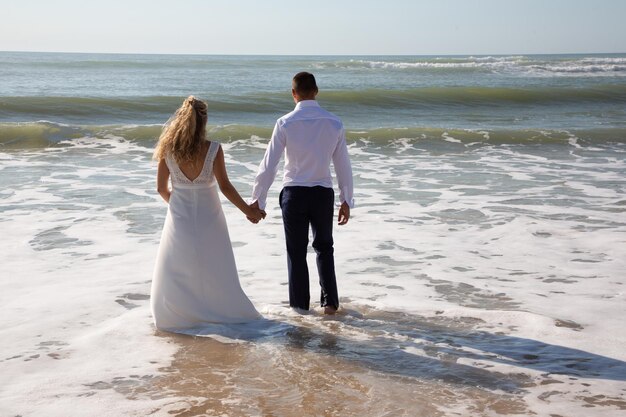 Sposa e sposo di nozze su un piede di spiaggia in acqua di mare