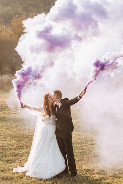 sposa e sposo giocando con il fumo colorato nelle mani viola abbracci e baci bombe di fumo ad un matrimonio