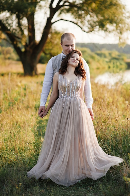 Sposa e sposo in posa attraverso il campo vicino al fiume