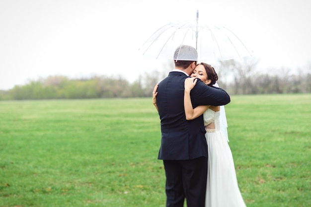 Sposa e sposo in un giorno di nozze piovoso che camminano sotto un ombrello