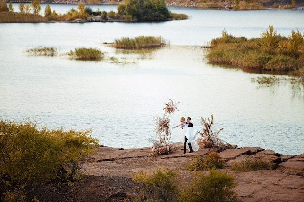 Sposa e sposo vicino alla decorazione di nozze a una cerimonia su una scogliera di roccia vicino all'acqua al tramonto