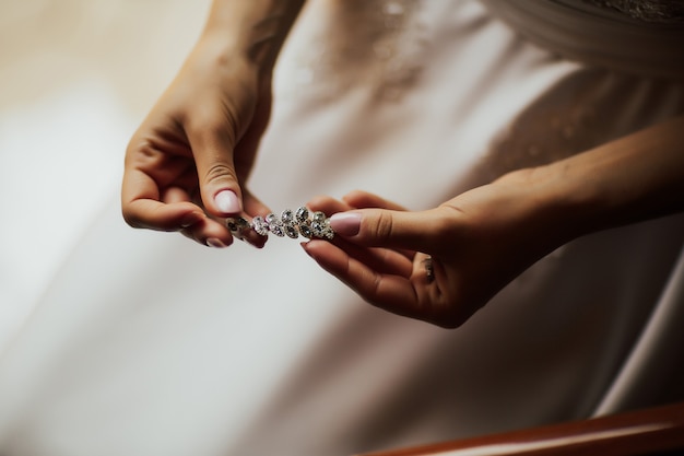 Sposa elegante che tiene orecchini d'argento. Mani con gioielli.