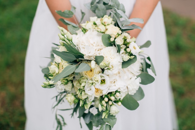 Sposa elegante in vestito da sposa bianco che tiene bello mazzo