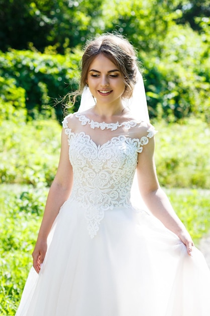 Sposa felice in un lungo abito da sposa bianco e velo in un parco verde sulla natura. Immagine del matrimonio di una giovane ragazza, trucco femminile e acconciatura. concetto di matrimonio