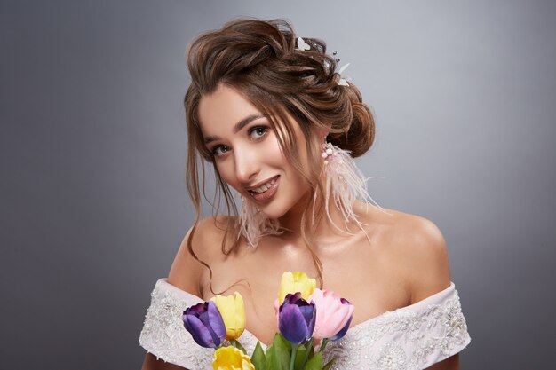 Sposa felice su sfondo grigio con fiori sorridenti