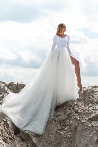 Sposa in abito bianco all'aperto sulla sabbia e sullo sfondo del cielo blu