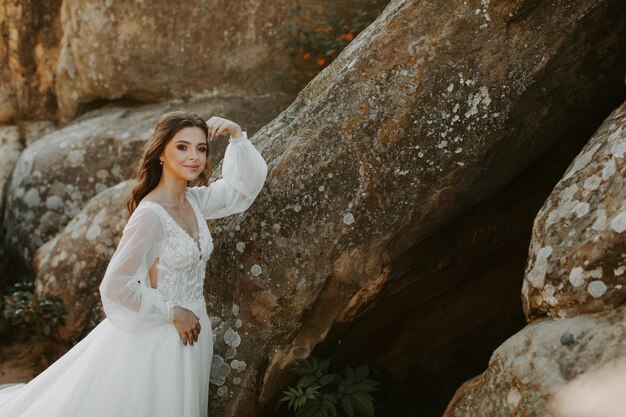 Sposa in abito bianco in piedi sulla collina e guardando il tramonto.