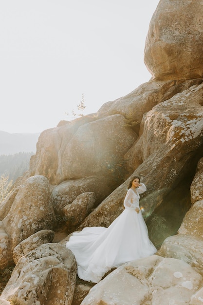 Sposa in abito bianco in piedi sulla collina e guardando il tramonto.