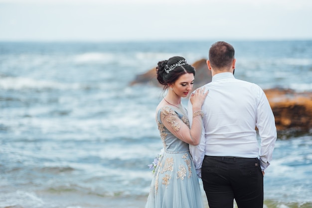 sposa in abito blu cammina lungo la riva dell'oceano