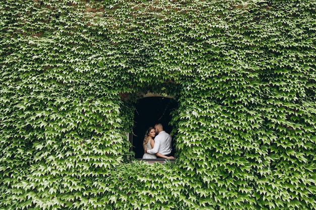 Sposa in abito da sposa bianco e sposo nella finestra dell'edificio completamente coperto di foglie