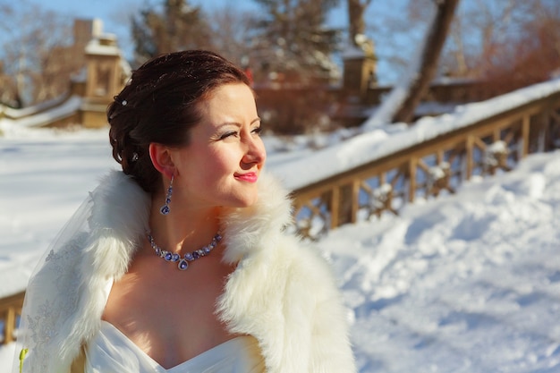 Sposa in posa nella foresta invernale in una pelliccia. Sessione fotografica di matrimonio in un parco innevato.