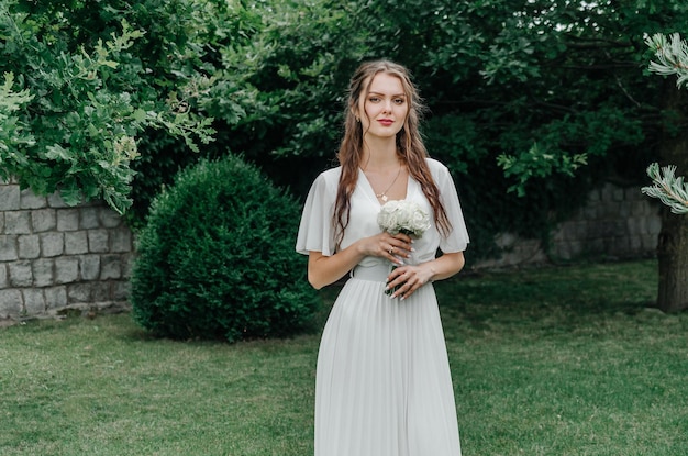 Sposa in un abito bianco con un bouquet da sposa bianco in natura