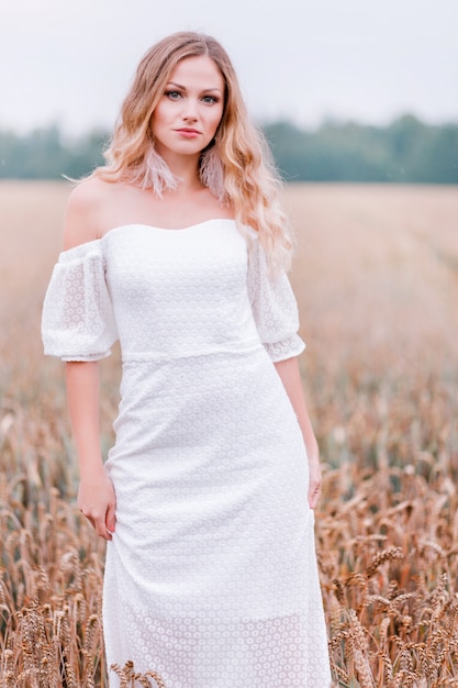 Sposa in un abito bianco in posa su un campo di grano