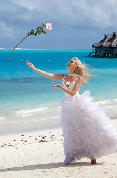 sposa in un abito lungo bianco getta una rosa su una spiaggia