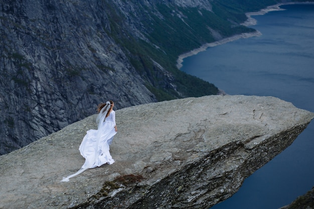 sposa in un lungo abito da sposa su un frammento di roccia di Trolltunga nelle montagne della Norvegia