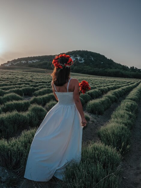 Sposa in un vestito bianco che tiene un mazzo di fiori di papavero caldo tramonto sullo sfondo del