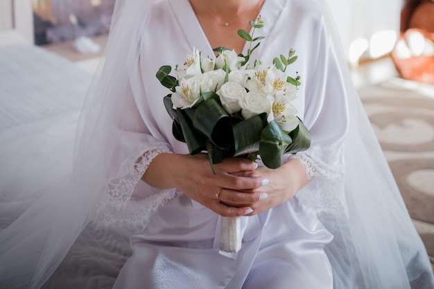 Sposa in vestaglia con in mano un bouquet al mattino