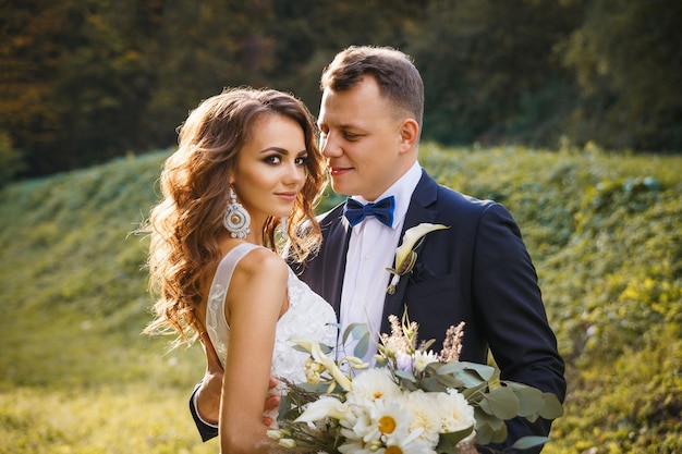 Sposa riccia elegante e sposo alla moda che abbracciano sul prato verde