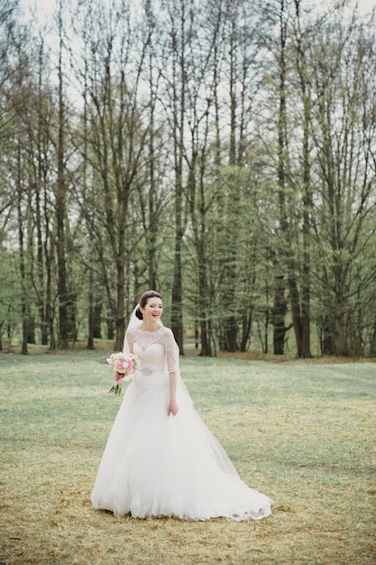 Sposa sorridente in un vestito bianco con un mazzo rosa. Matrimonio in primavera