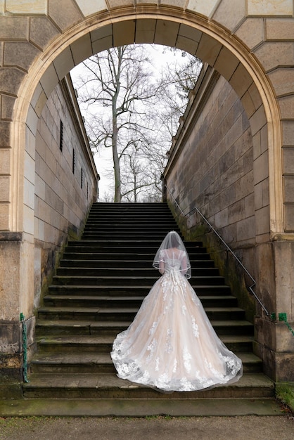 Sposa sui gradini di pietra di un antico edificio in un arco Vista posteriore da dietro Matrimonio