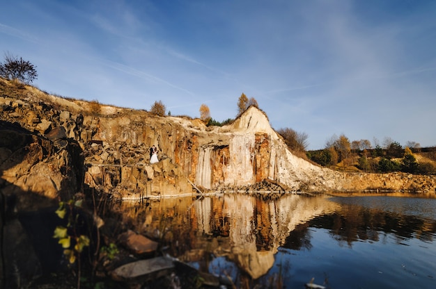 Spose in piedi e baciare le rocce marroni e il lago