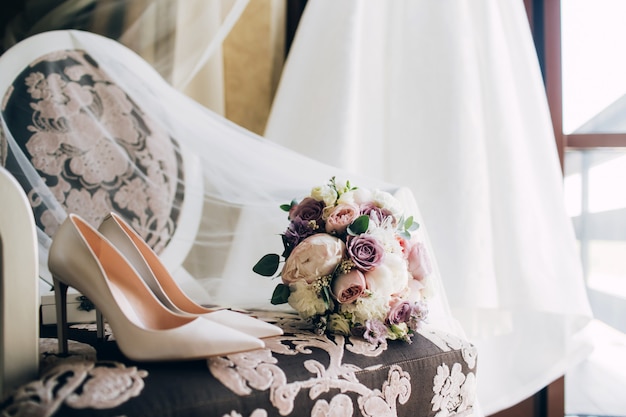 Spose scarpe da sposa con un mazzo di rose e altri fiori sulla poltrona