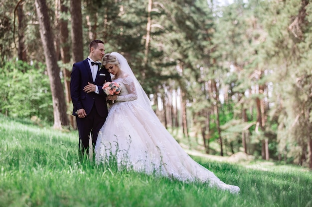 sposi emotivi nel parco verde in spring.portrait della sposa e dello sposo in una giornata di sole all'aperto. sposa e lo sposo che abbraccia e sorride al giorno delle nozze in natura. Bellissimi sposi camminano all'aperto