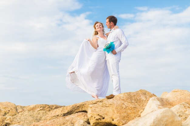 Sposi in piedi sulla scogliera. Lo sposo abbraccia teneramente la sposa.