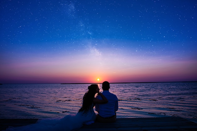 Sposi novelli sull'oceano al tramonto. una coppia innamorata solo che ha celebrato il matrimonio in abiti da sposa sta su un ponte di legno nel mare sullo sfondo di un bellissimo tramonto.