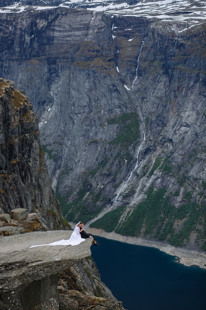 sposi seduti su un frammento di roccia in montagna, sullo sfondo del fiordo