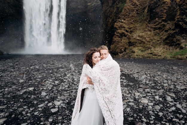 Sposi vicino alla cascata skogafoss la sposa e lo sposo coperti con una coperta di lana dove