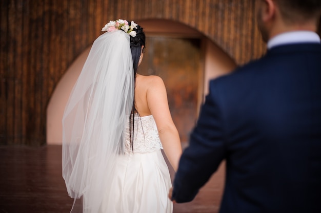 Sposo in un abito seguendo la sua bellissima sposa vestita con un abito bianco