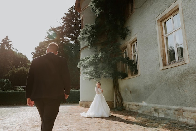 Sposo sensuale bello che abbraccia la sposa appena sposata da dietro al vecchio castello