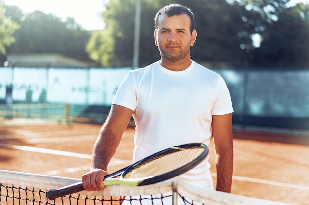 Spoty uomo con racchetta da tennis in piedi sul campo in terra battuta vicino a rete