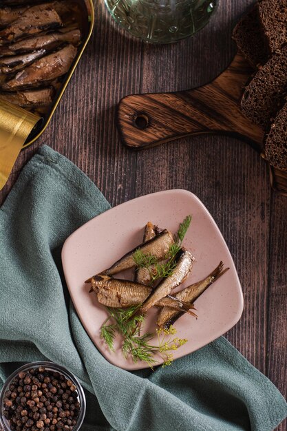 Sprat affumicati in scatola in olio e su un piatto sul tavolo e vista verticale