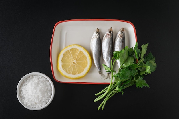 Spratto salato con prezzemolo e limone su un tavolo nero Delizioso antipasto di mare Piatto lay